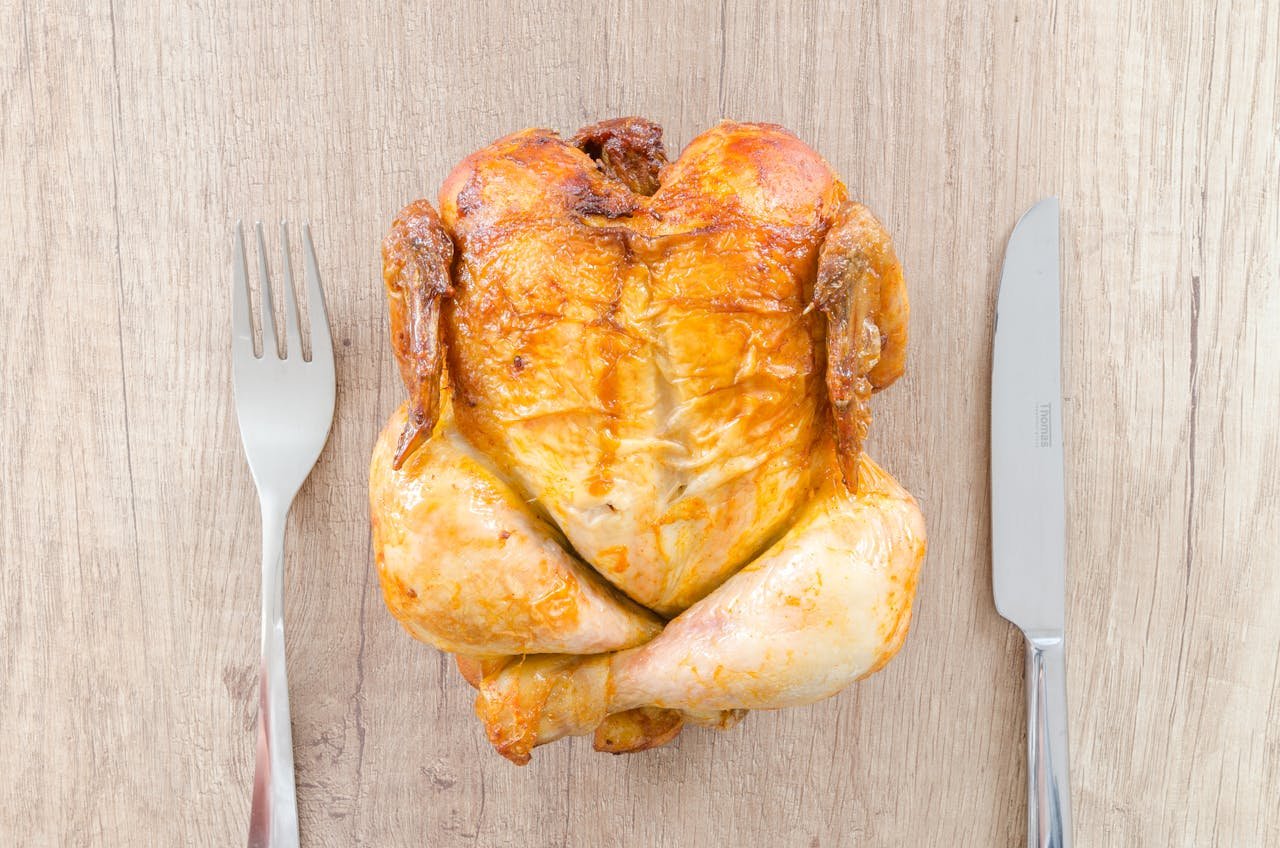 Mastering the First Impression: Your intriguing post title goes here Top view of a perfectly roasted chicken placed between fork and knife on a wooden table.